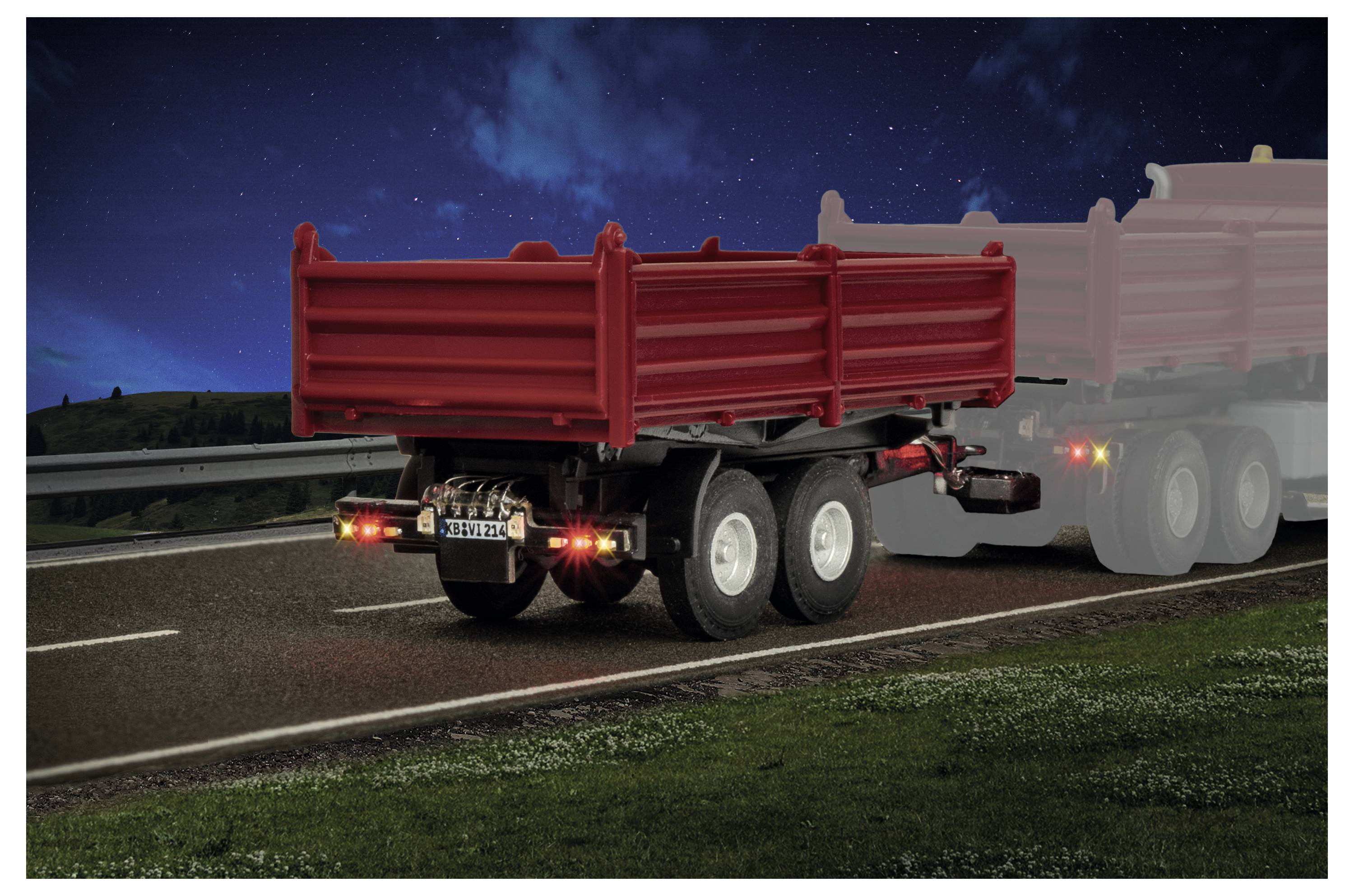 Röd dumpbilssläp som kör på natten på en motorväg, med baklampor synliga och en andra ljus släpvagn delvis synlig bakom den.