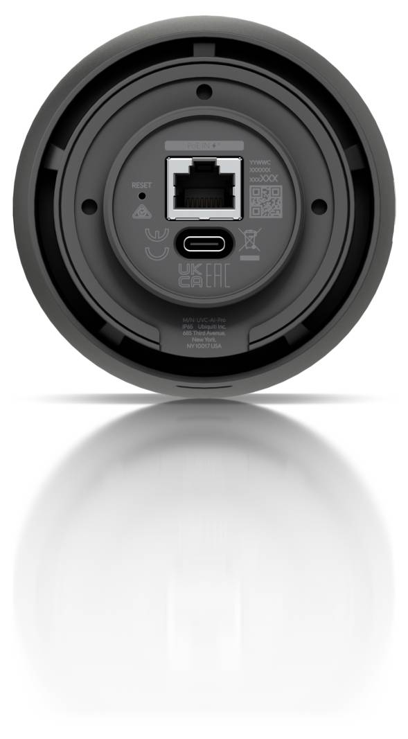 Toppvy av en cirkulär enhet som visar en Ethernet-port och USB-C-port i mitten, med subtilt tryckta ikoner och etiketter på ett mörkgrått hölje.