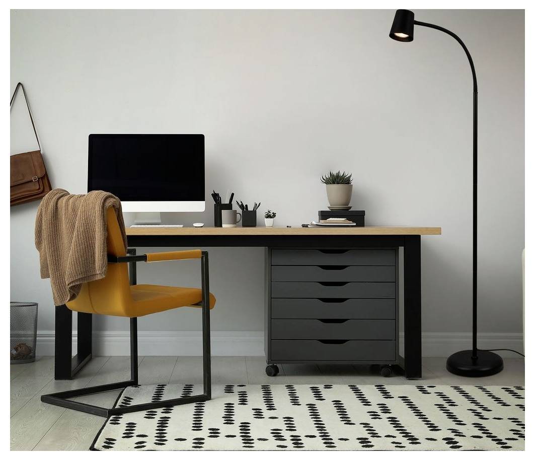 Minimalistiska hemmakontor med skrivbord, dator, senapsfärgad stol, golvlampa och mönstrad matta mot en vit vägg.