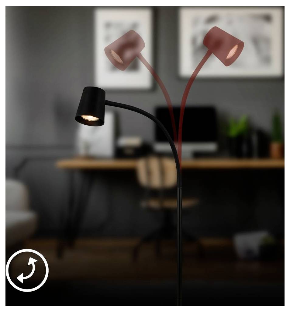 Svart justerbar skrivbordslamp med två rödtonade huvuden, ett tänt, med suddig hemmakontorsbakgrund med skrivbord och stol.