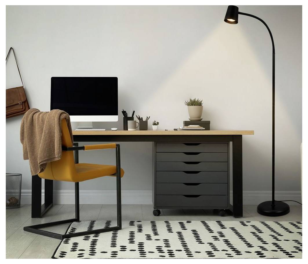 Modernt hemmakontor med ett skrivbord, datorskärm, gul stol med ett kastat täcke, golvlampa och mönstrad matta.