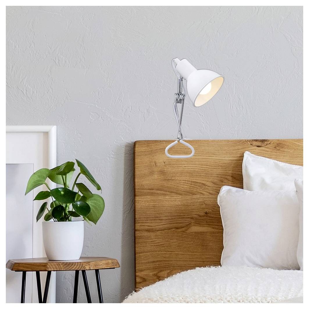 Sovrumshörn med träsänggavel, belyst vägglampa, vitt sängöverkast och en kruka på ett litet bord.