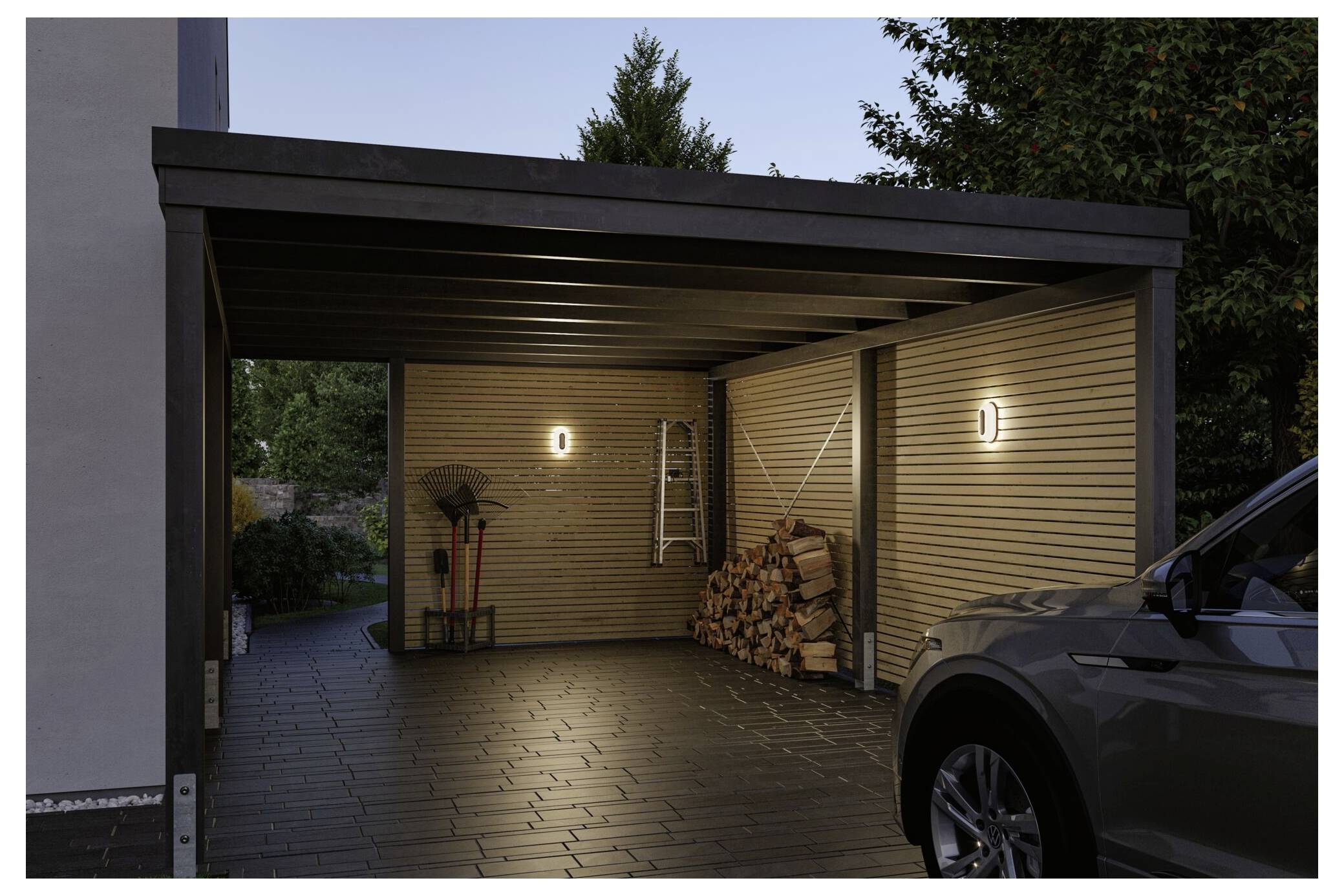 Modern carport i skymningen med två väggljus, staplade ved, en stege och en parkerad bil framför.