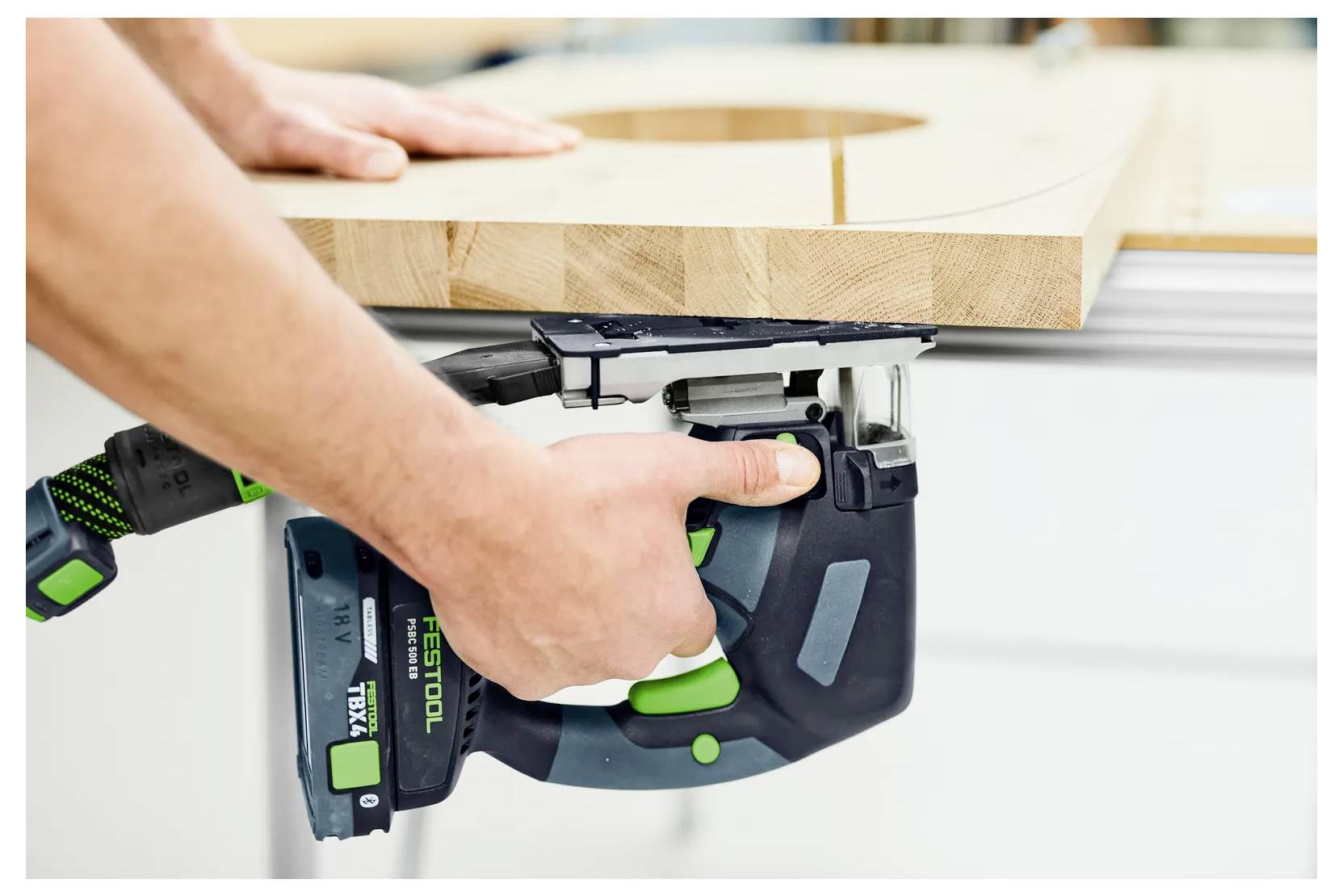 En person använder en Festool-elsåg för att såga kanten på en träbräda på en arbetsbänk.