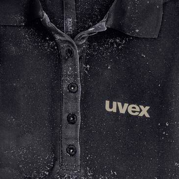 Närbild av en svart knappskjorta med "uvex"-logotypen på bröstet, prickad med damm eller pulver.
