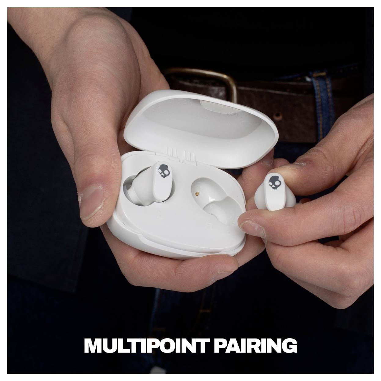 Händer som håller ett vitt laddningsfodral för öronsnäckor och två öronsnäckor, med texten "MULTIPOINT PAIRING" längst ned.