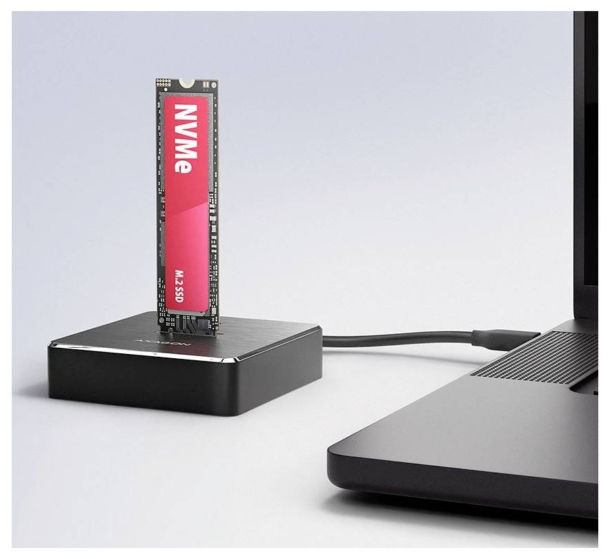 NVMe M.2 SSD installerad upprätt i ett litet externt hölje bredvid en bärbar dator, ansluten via kabel, som visar en bärbar lagringsuppsättning.