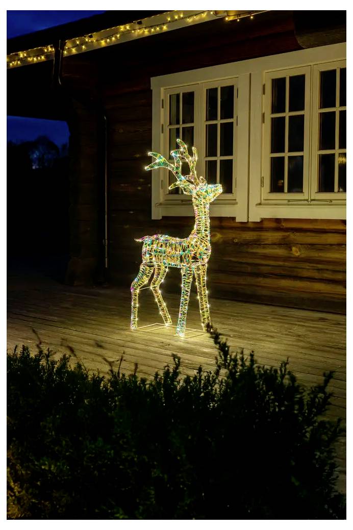En lysande trådram-ren som juldekorationsstycke står på en träveranda bredvid ett hus på natten.