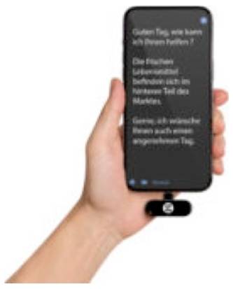 Hand som håller en smartphone i mörkt läge med suddig tysk text, med ett litet bifogat tillbehör längst ned på telefonen.