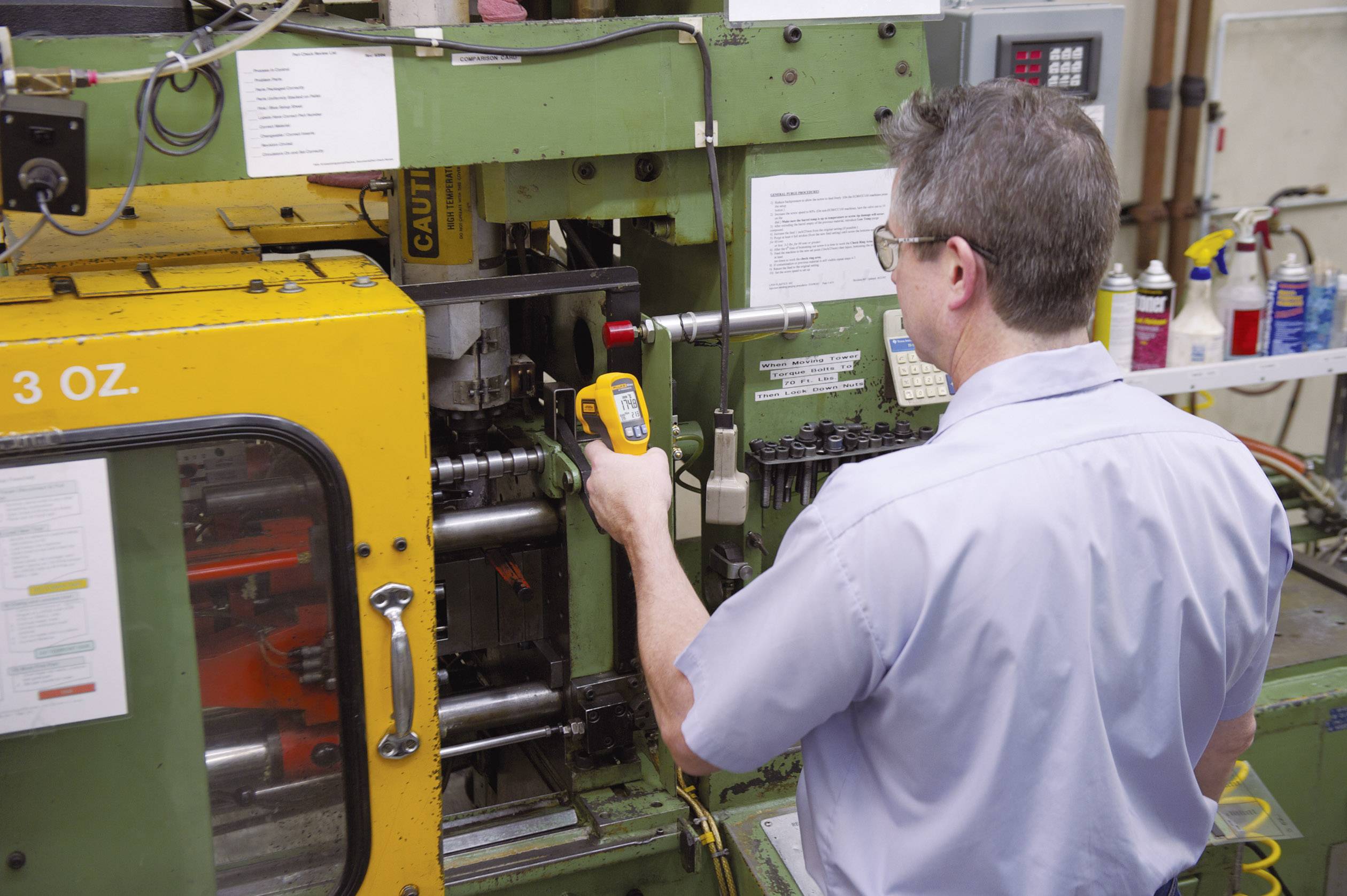 En man betjänar en stor industriell maskin i en fabrik. Han använder ett mätinstrument för att utföra en kontroll.