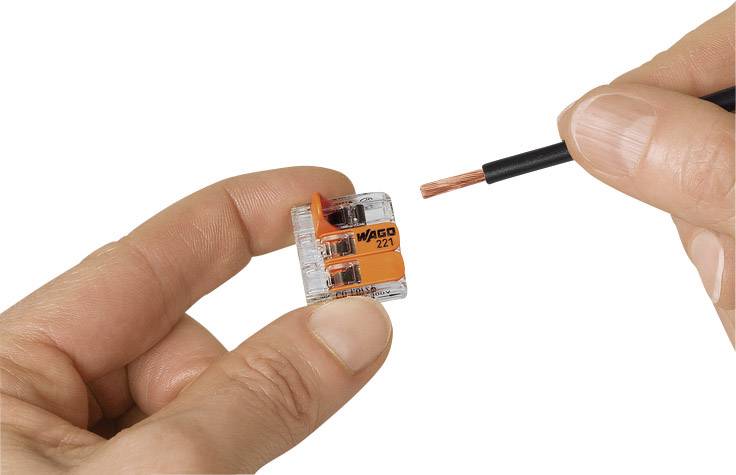 En hand håller en transparent WAGO 221-klämmа medan en tråd med blank ände sticks in i klämman.