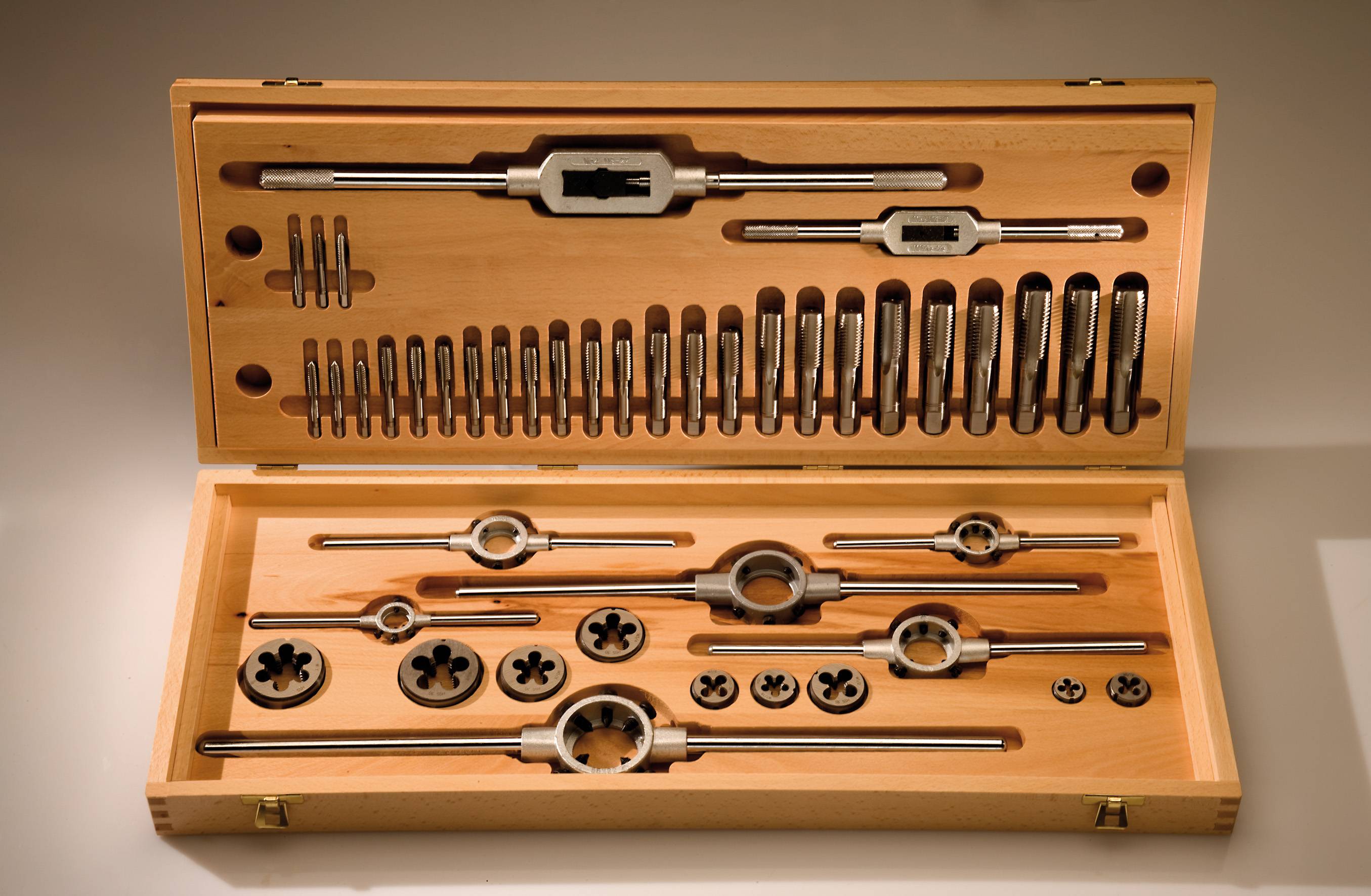 En uppsättning metallgängborrar och gängsnitt i en öppen trälåda, sorterade efter storlek och form för precisionsmetallbearbetning.