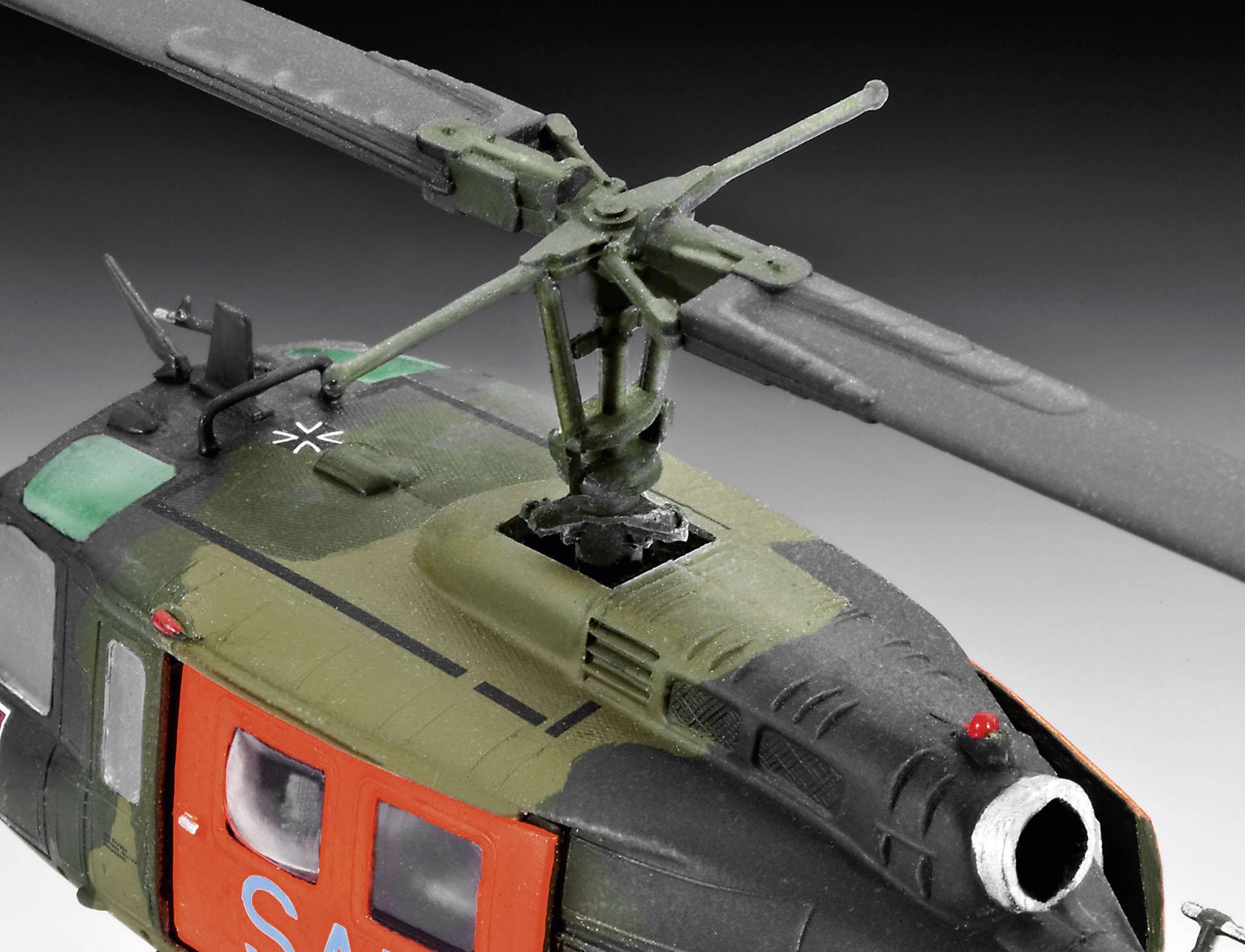 Bilden visar en modell av en militärhelikopter i kamouflagefärger med tydliga rotorblad och ett cockpit i lysande orange.