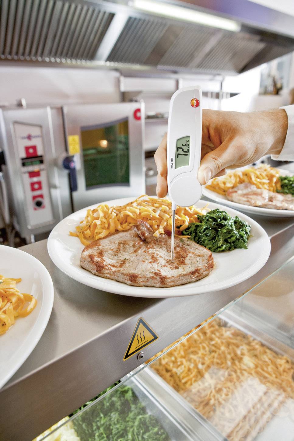 En tallrik med stekt kött, spätzle och spenat mäts med en termometer. Temperaturen uppgår till 72,6 °C. Bakgrund: Kök.