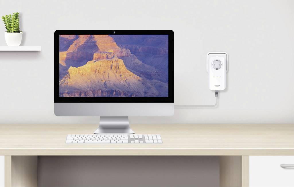 En dator på ett bord med en skärm som visar Grand Canyon. Bredvid är en vit strömadapter ansluten till väggen.