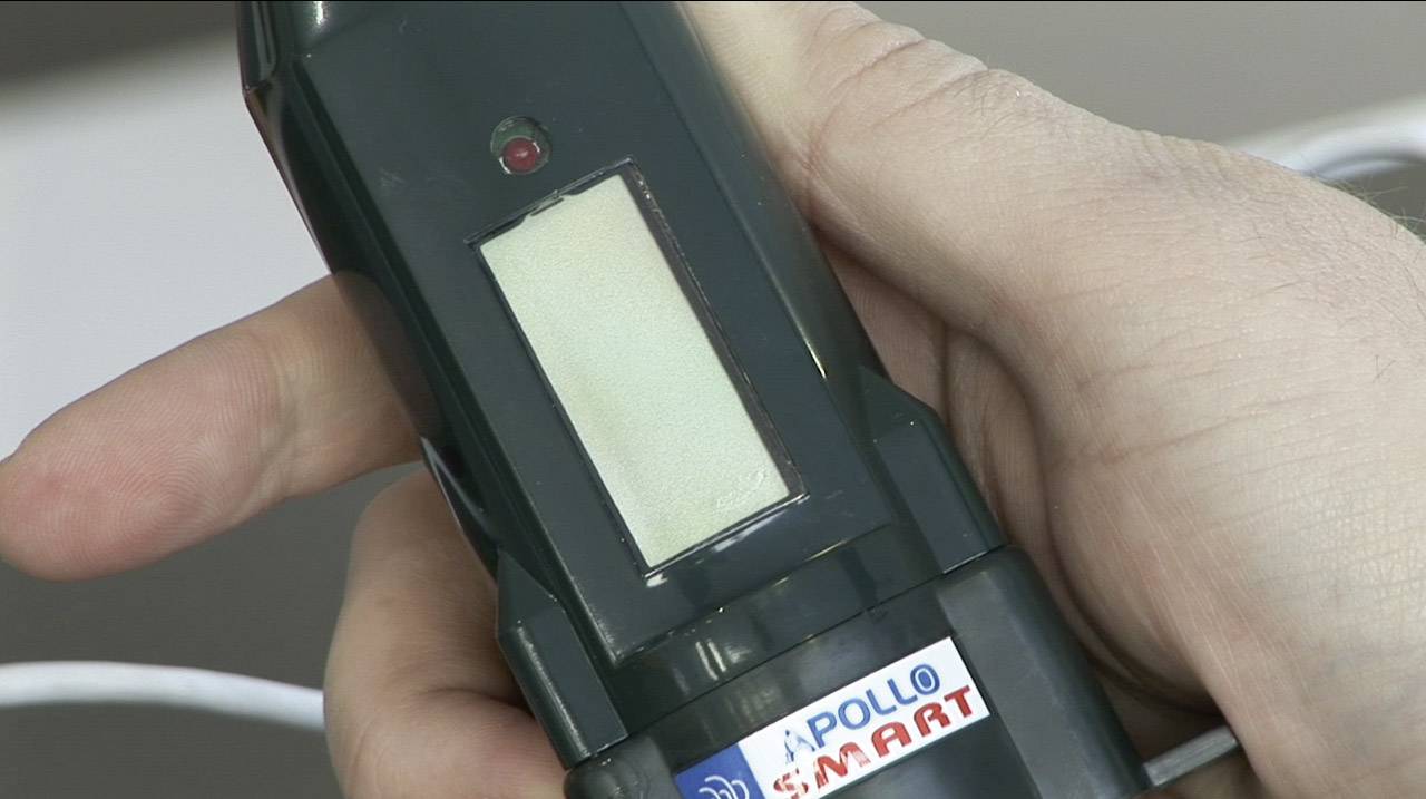 En hand håller en elektronisk enhet med en skärm. På enheten står det 'APOLLO SMART'.