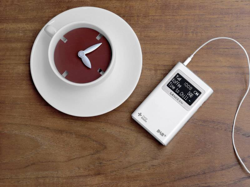 Kopp med klocka i mitten på ett fat, bredvid en MP3-spelare med hörlurar som visar spårinformation på displayen.