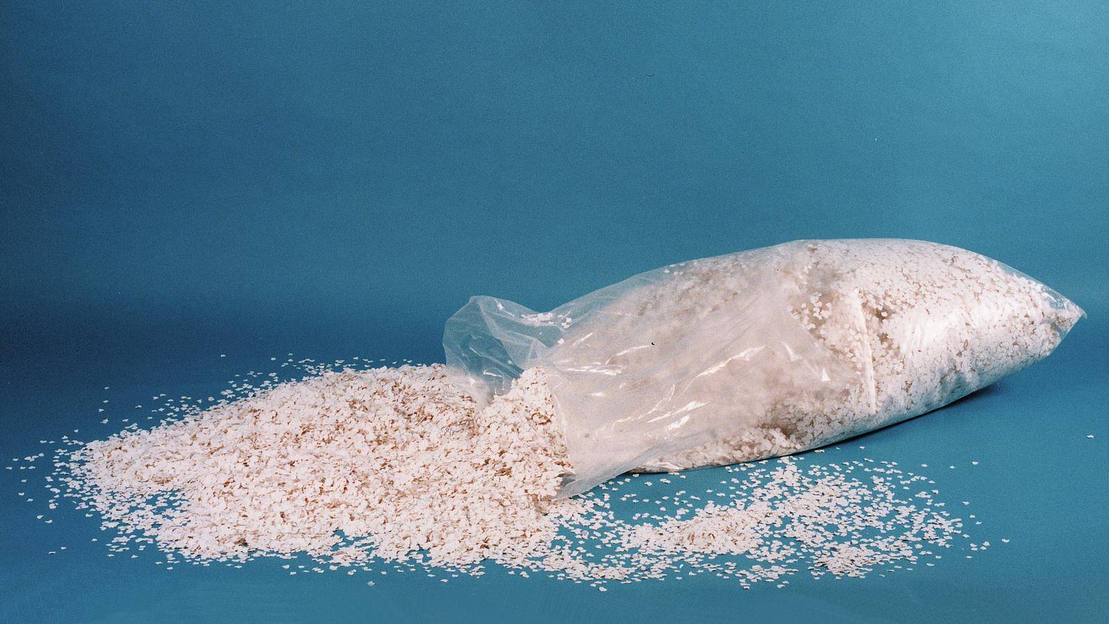 En öppnad plastpåse med perlit sprids ut på en blå yta. Perlit används ofta som jordförbättringsmedel.