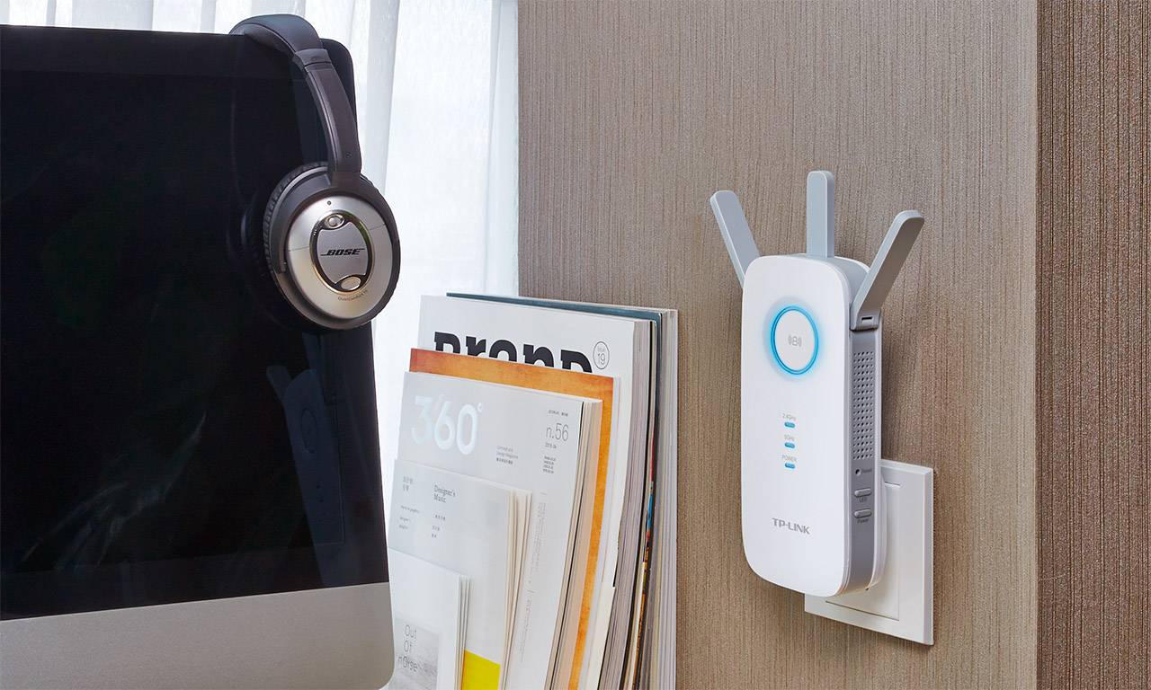 En WLAN-förstärkare är ansluten till ett vägguttag. Placerad bredvid en uppfälld laptop och ett headset på ett bord.