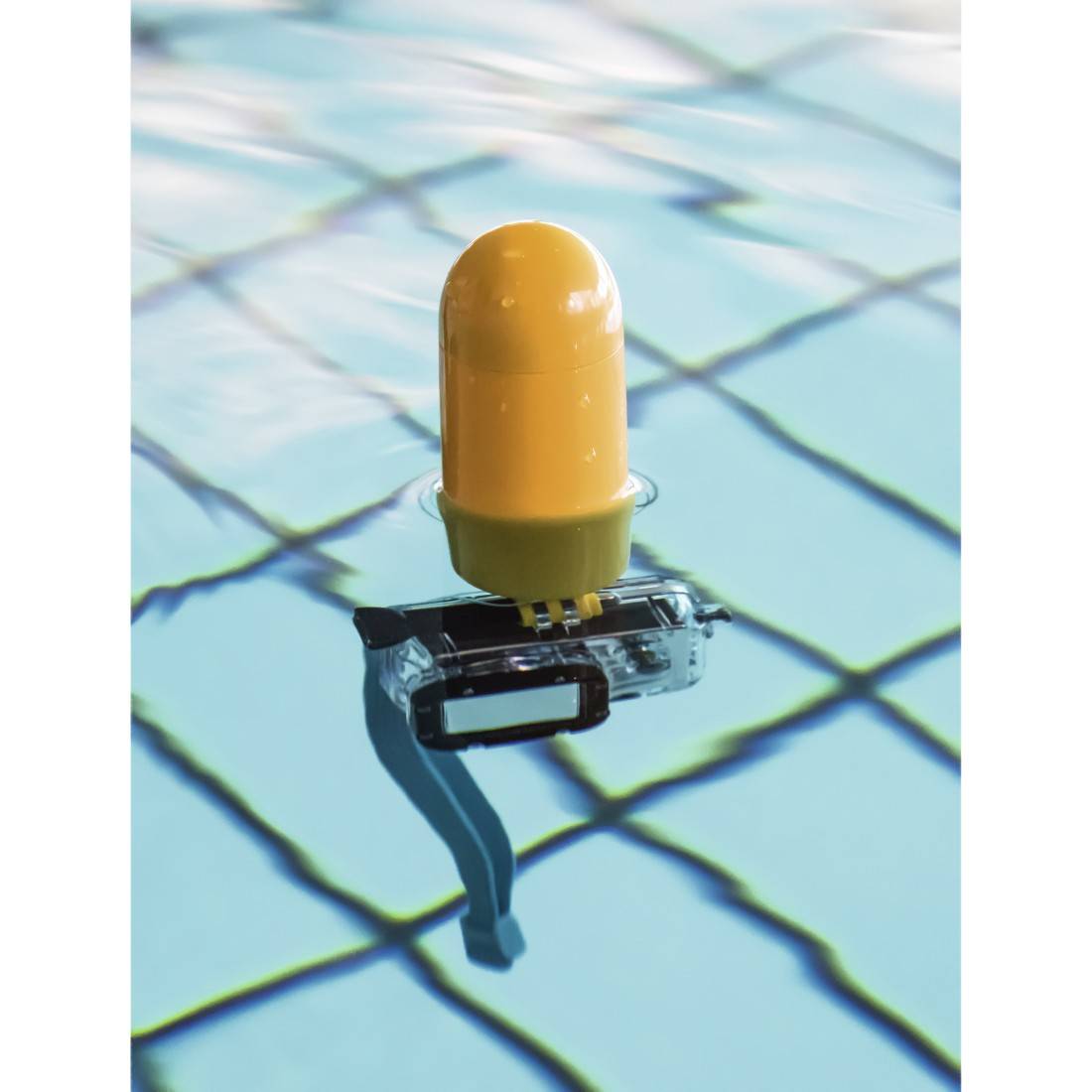 En gul dykarkapsyl flyter ovanför ett blått kakelmonster i en pool.