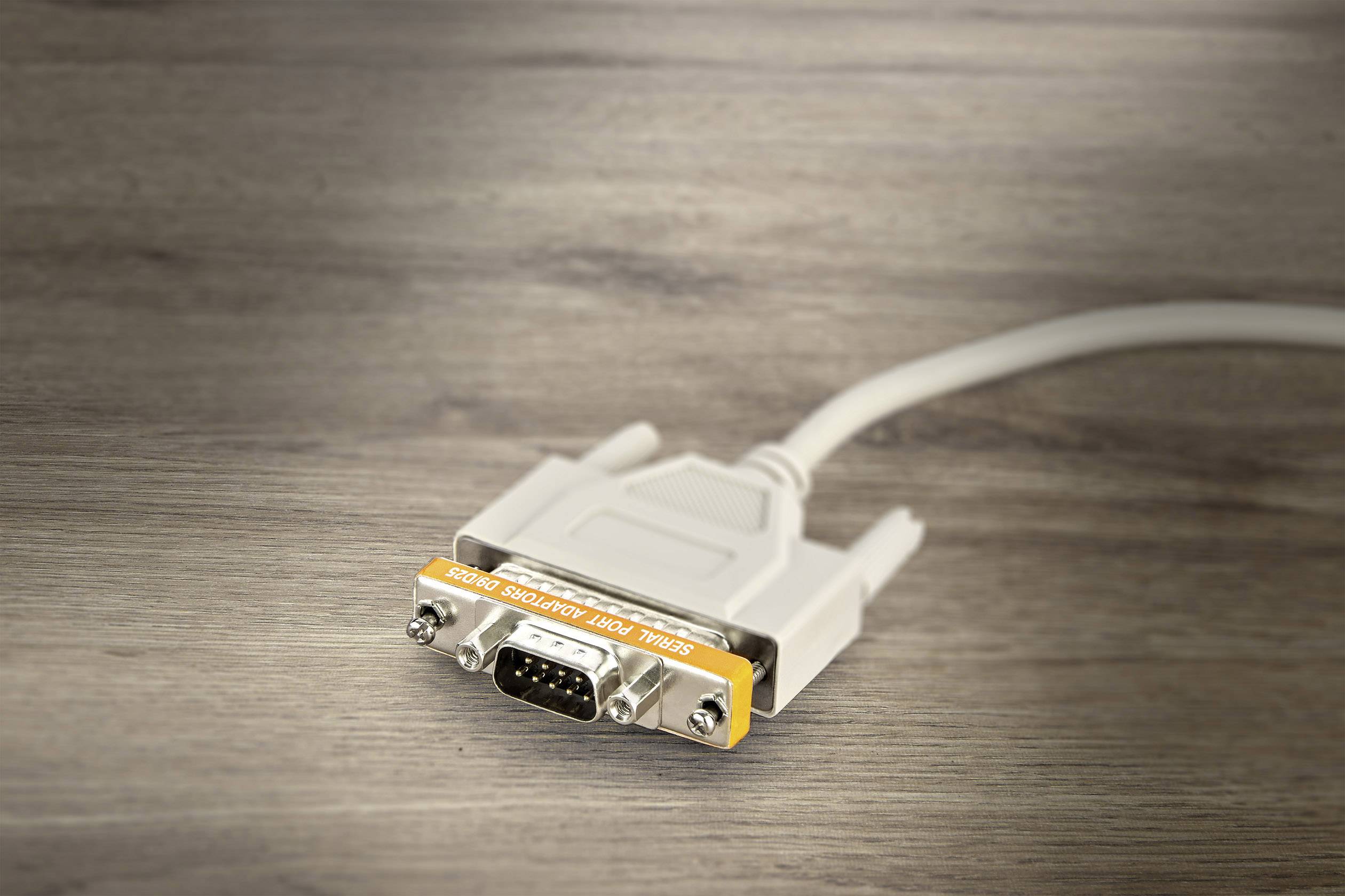 Ett grått VGA-kabel med en gul kontakt ligger på ett träbord.