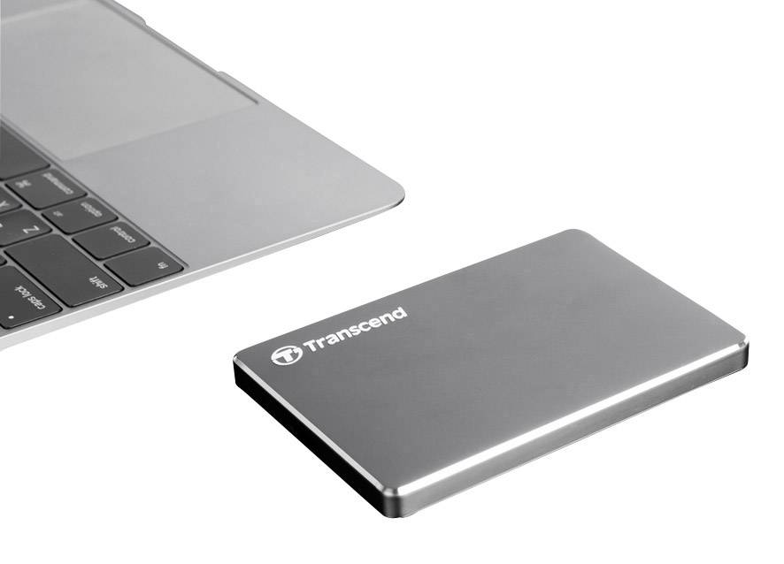 Extern hårddisk bredvid en bärbar dator, båda i silver. Hårddisken är tunn och kompakt, märket 'Transcend'.