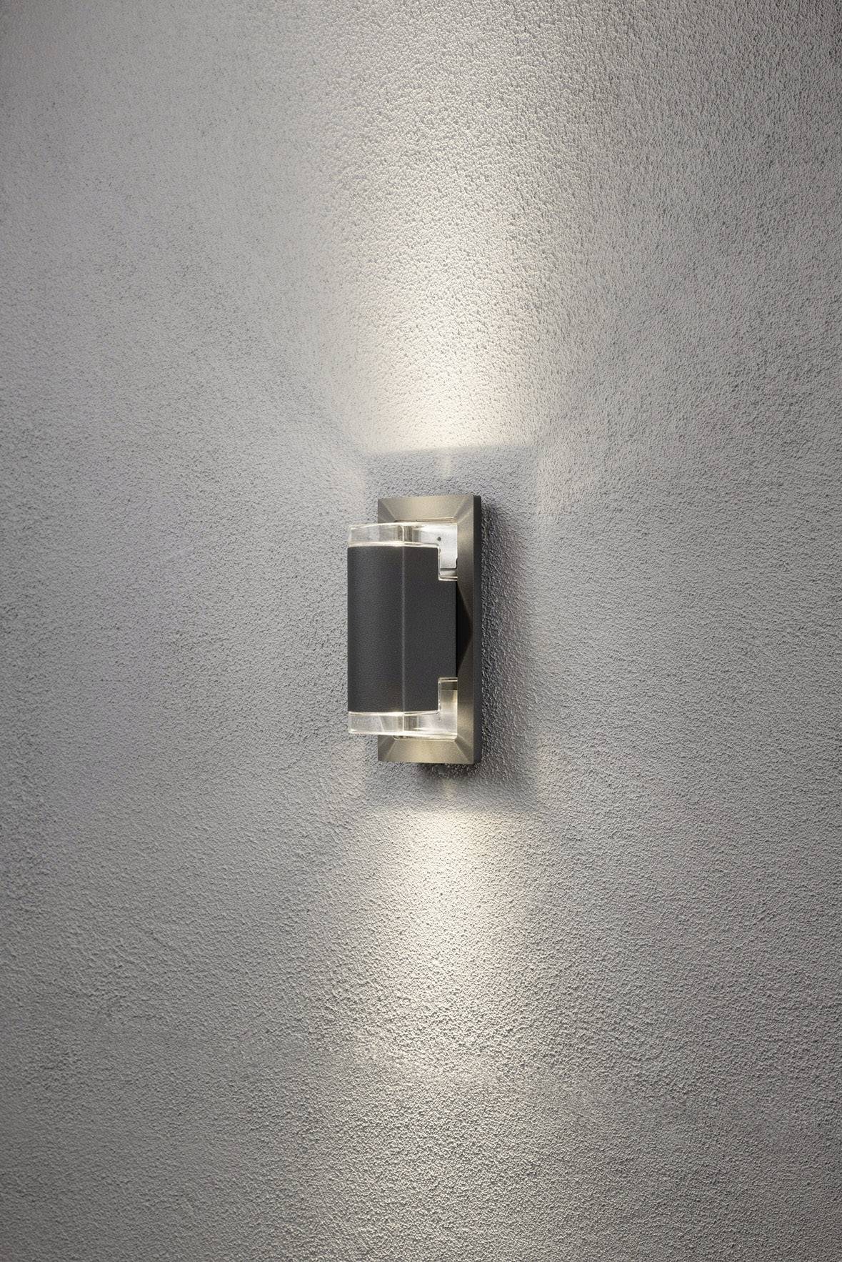 Vägglampa på en grå vägg, kastar diffust ljus uppåt och nedåt för stämningsfull belysning.