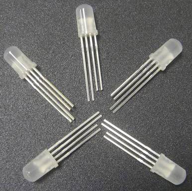 Fem transparenta LED-lampor, var och en med fyra långa metallstift, placerade i en cirkelformad formation på en mörk yta.