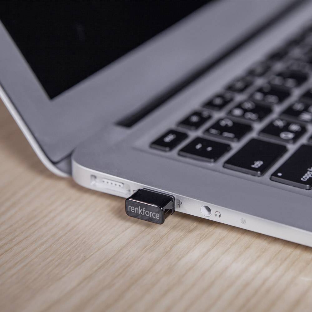 En USB-sticka från renkforce är ansluten till en bärbar dator som ligger på ett träbord. En del av datorns tangentbord är synligt.