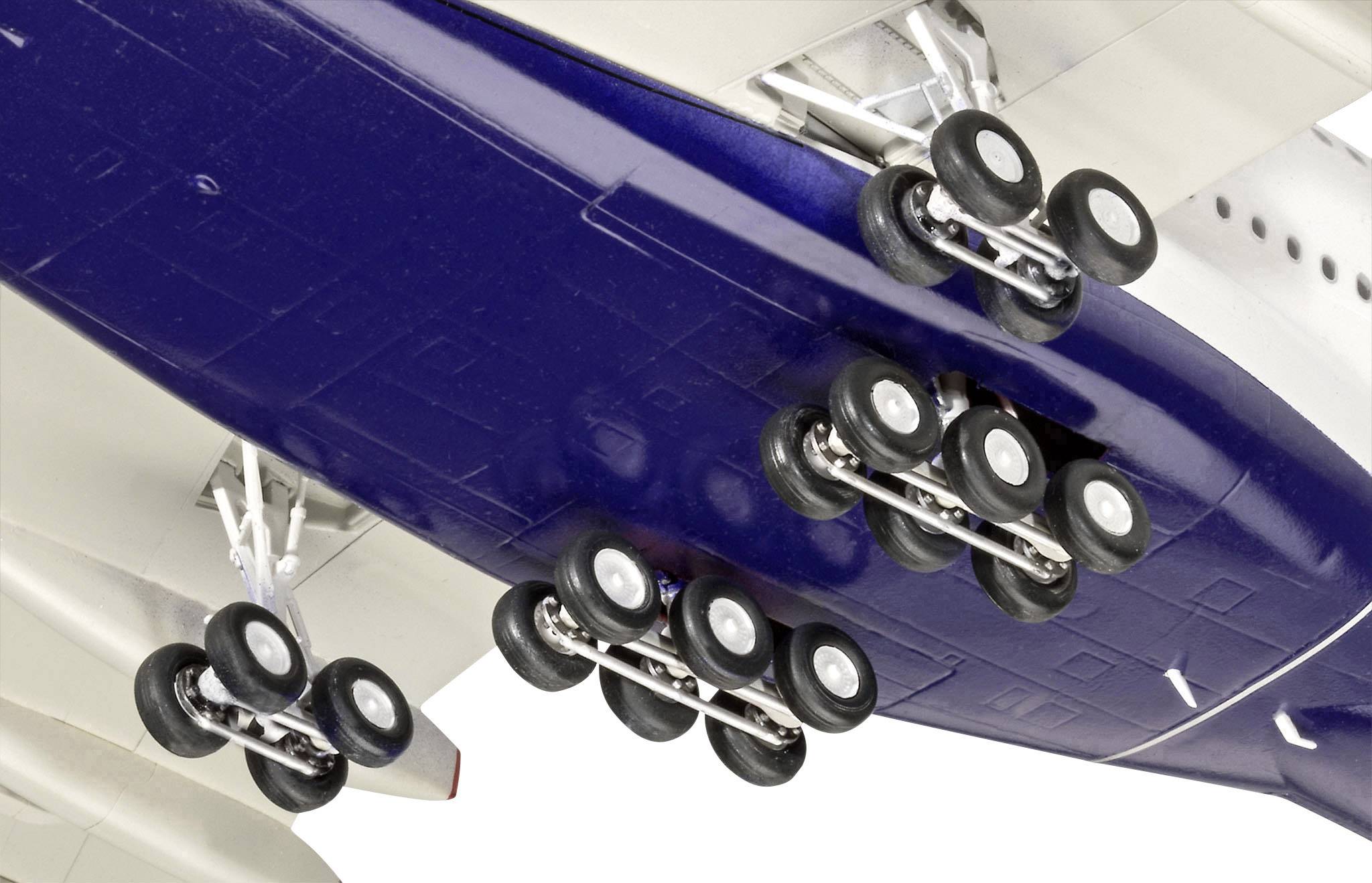 Närbild av ett flygplans landningsställ med flera hjul utfällda under flygkroppen. Rött och blått färgschema.