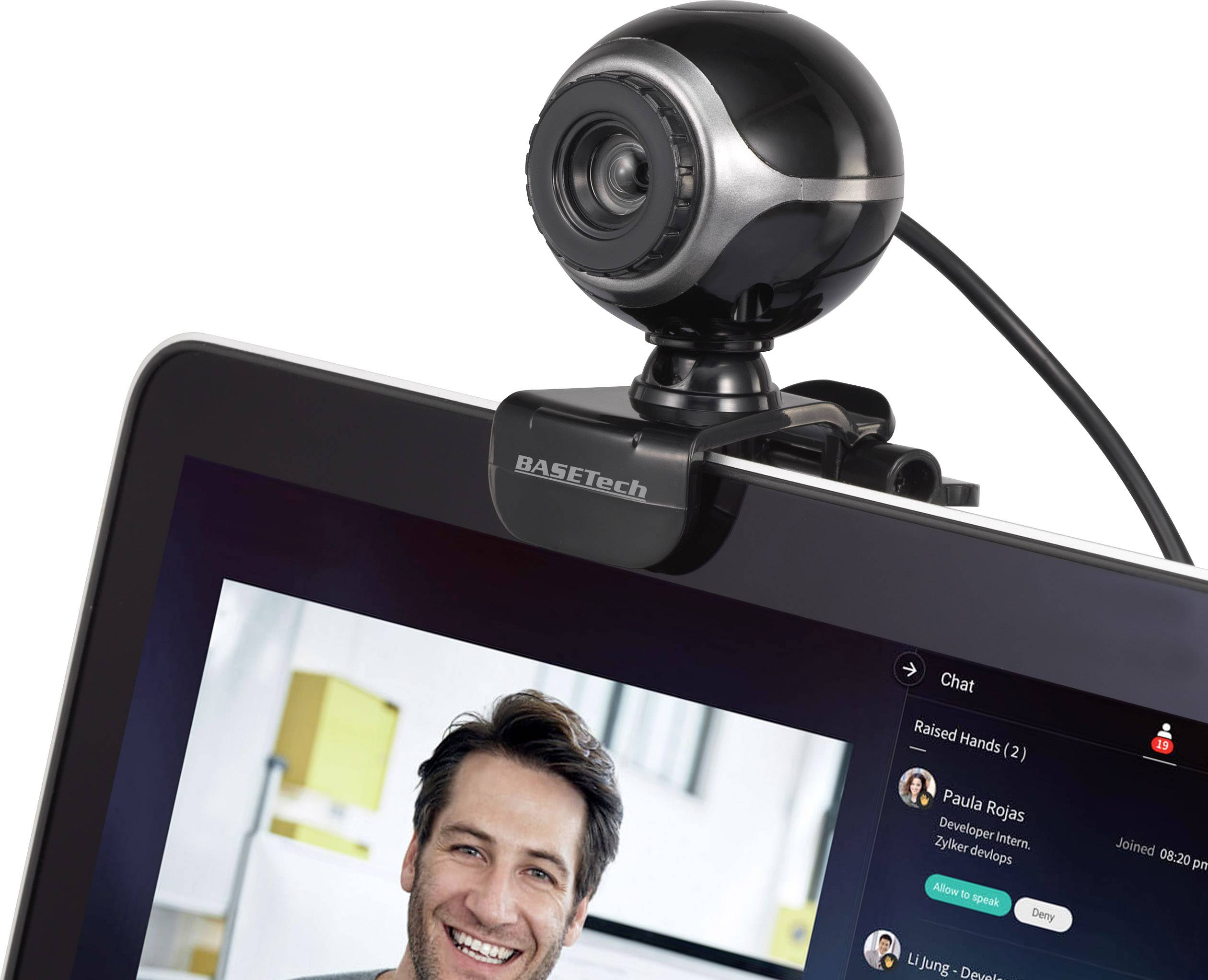 Webbkamera placerad längst upp på en skärm, visar en videokonferens med en man på skärmen och namnbeteckningar i chattfönstret.