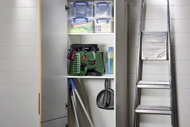 Ett öppet skåp visar verktyg, rengöringsmedel och välordnade lådor. Bredvid lutar en aluminiumstege mot väggen.