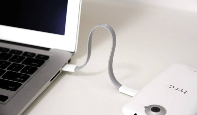 En bärbar dator är ansluten till en smartphone via en grå USB-kabel som är lätt böjd.