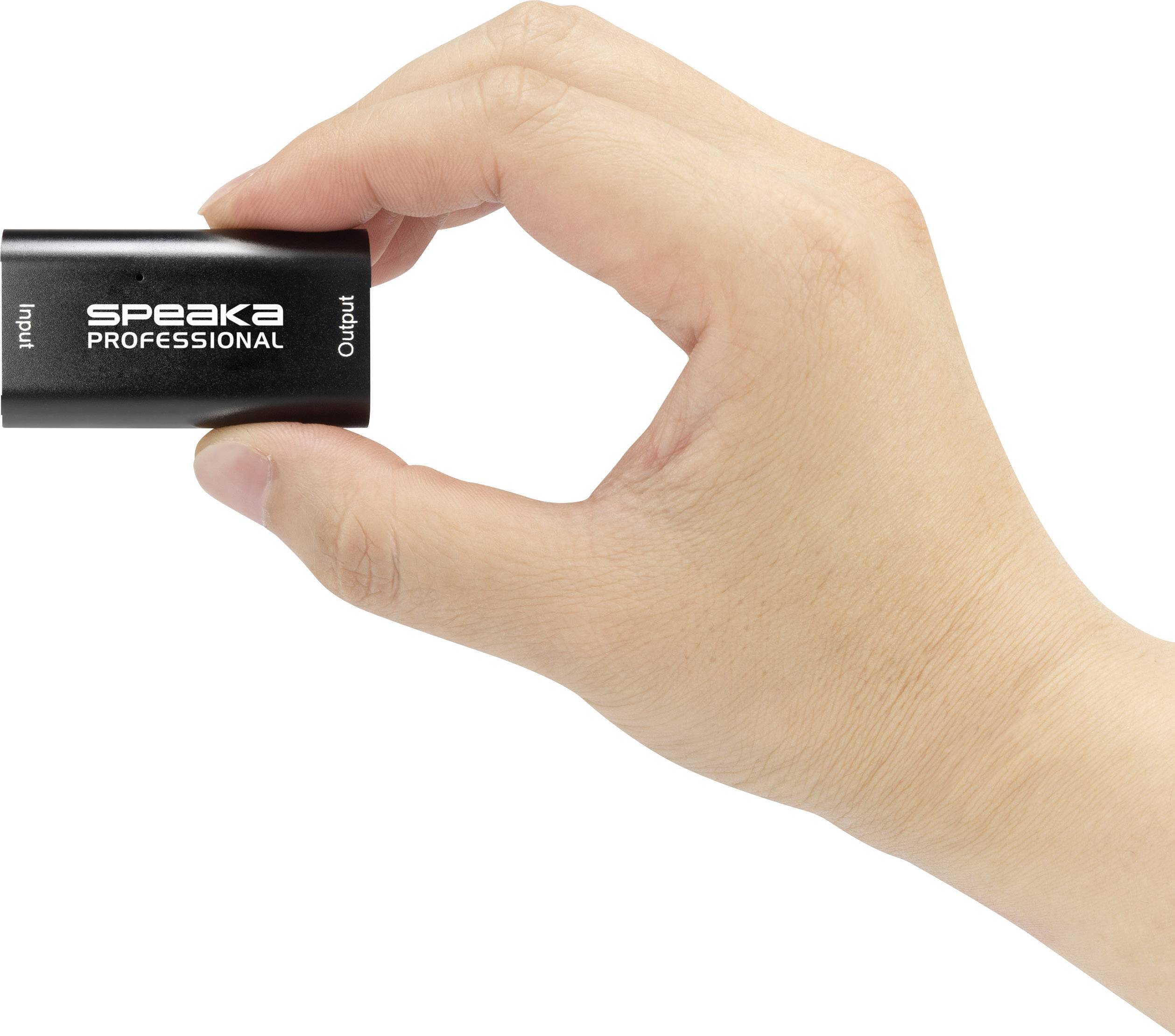 En hand håller en liten svart adapter märkt 'Speaka Professional', där portarna 'Input' och 'Output' är synliga.