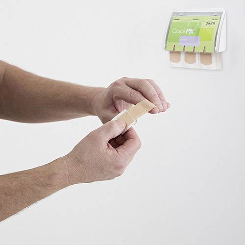 En person sätter ett plåster på fingret, framför en vägg med plåsterdispenser.