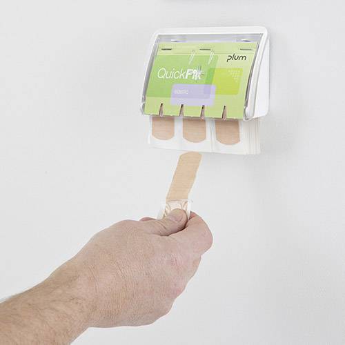 En hand drar ut ett plåster från en väggmonterad dispenser märkt 'QuickFix'. Dispensern är monterad på en vit vägg.