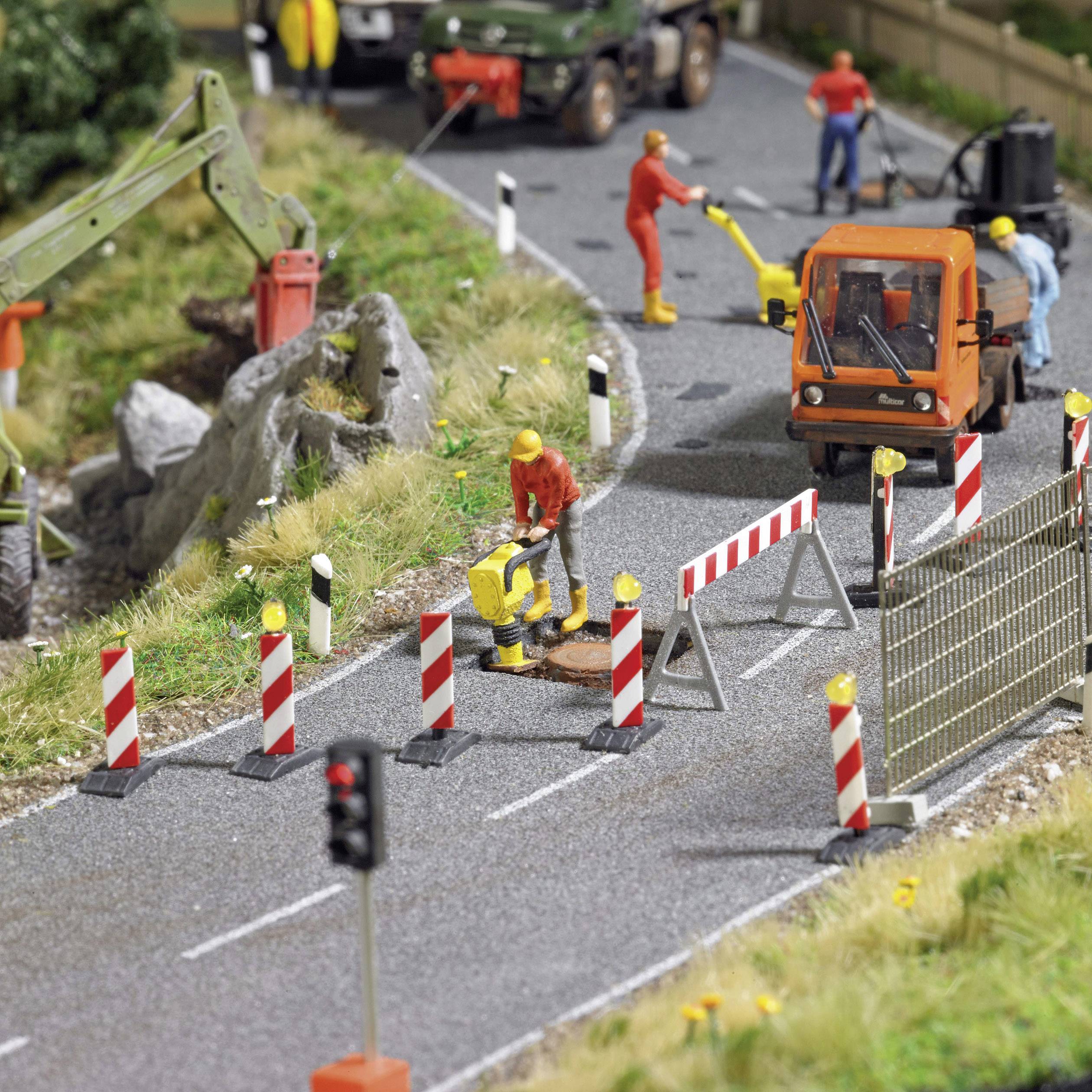 Miniatyrarbetsplats med en orange klädd arbetare som manövrerar maskiner, omgiven av avspärrningar och två fordon på en väg.