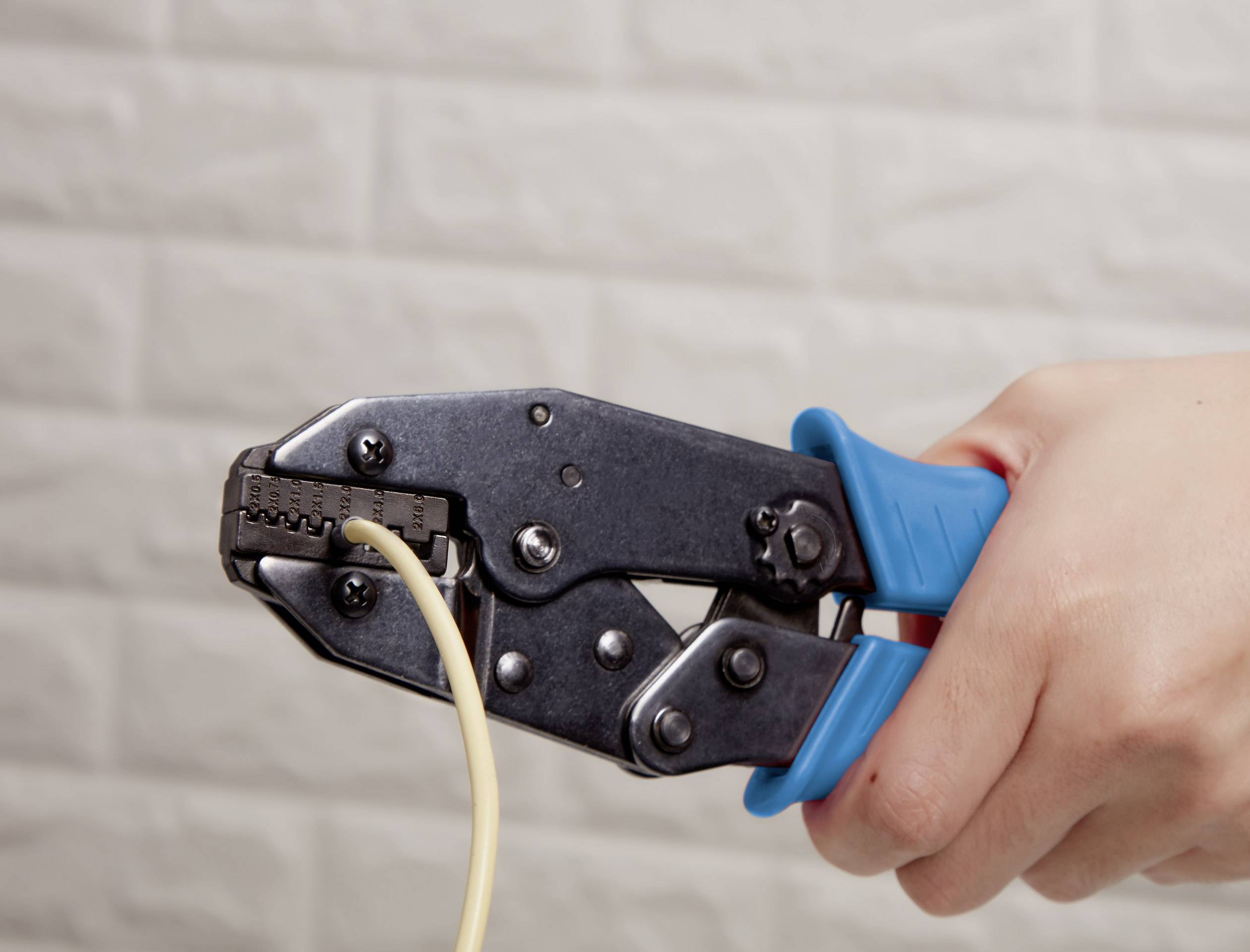 En person håller en crimptång som förbinder en kabel med en kontakt. Tången har blå handtag.