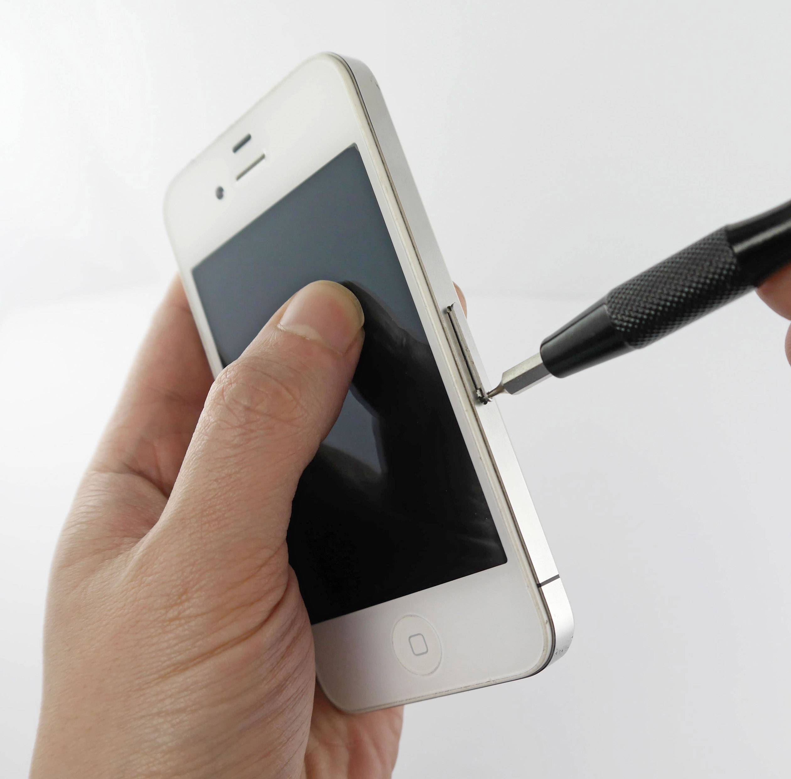 En hand håller en smartphone medan en annan hand arbetar med en svart skruvmejsel vid sidan av telefonen.