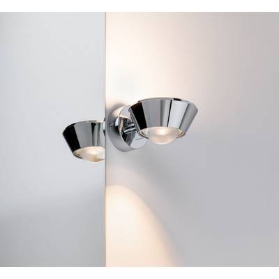Modern vägglampa med glänsande kromfinish monterad på vit vägg, ser stilfull ut och ger ett varmt ljus.