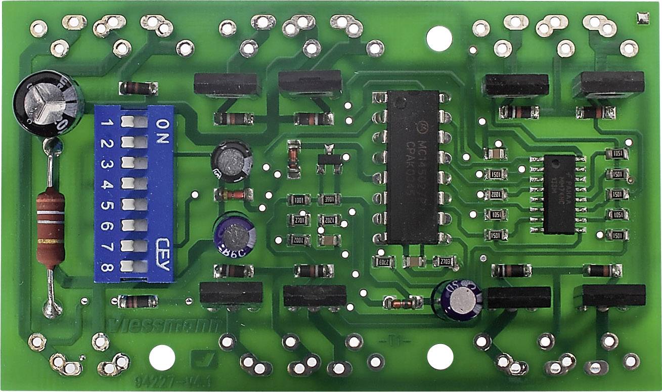 En grön kretskort med elektroniska komponenter, inklusive motstånd, kondensatorer och en DIP-switch märkt 'ON'.