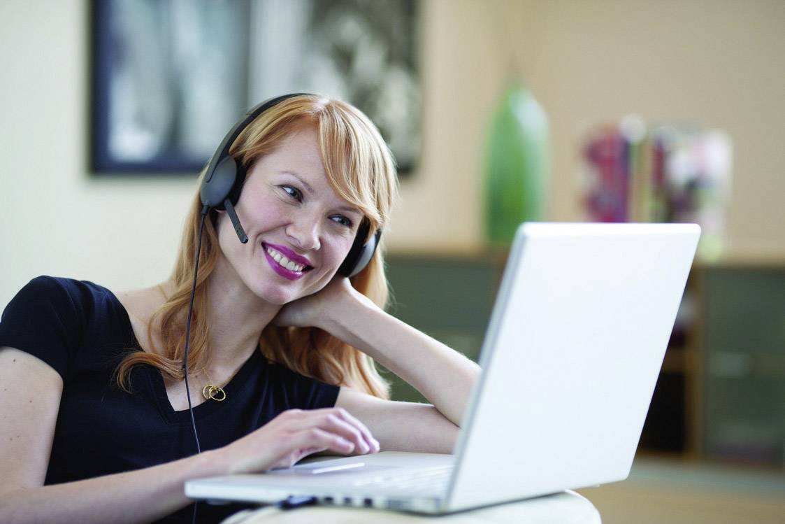 En leende person med headset sitter framför en laptop och verkar delta i ett virtuellt möte.