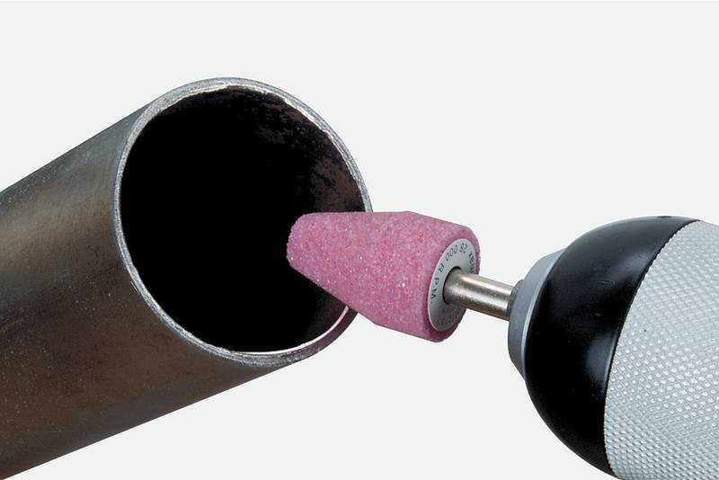 En borr med ett rosa slipverktyg bearbetar insidan av ett metallrör och visar användningen av slipverktyg vid metallarbete.
