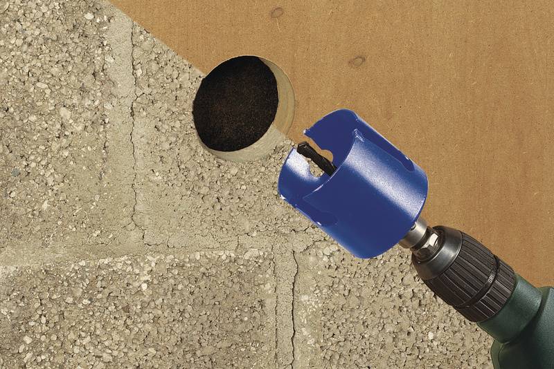 En borr med ett blått fäste borrar ett runt hål i en betongvägg. Borren är delvis synlig på höger sida.