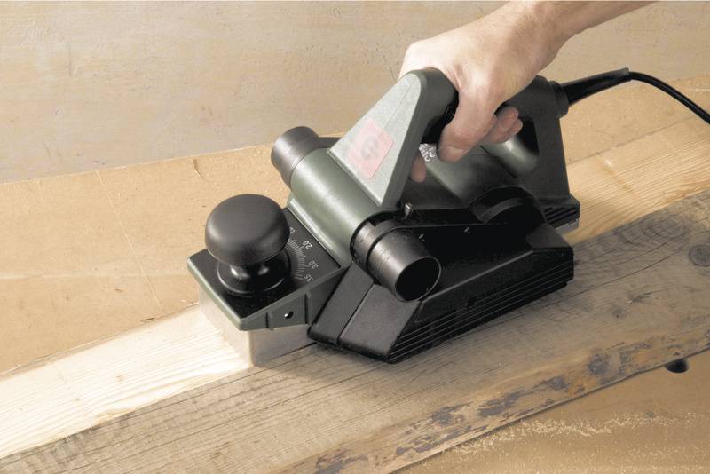 En person hyvlar ett trästycke med en elektrisk hyvel.