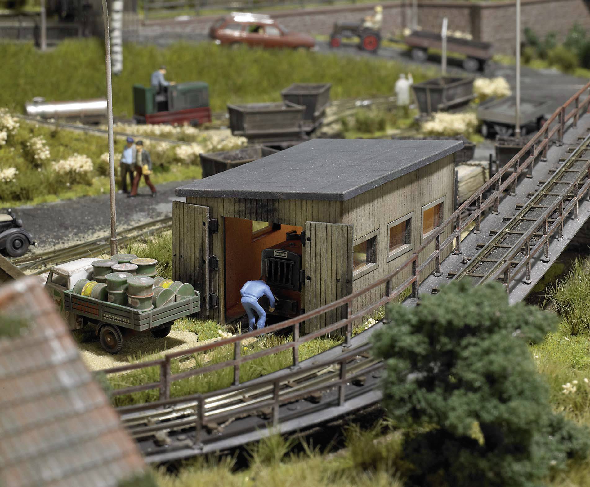 Miniatyrmodell av en lantlig järnvägsscen med hus, transportfordon och figurer. I förgrunden ligger en bro.