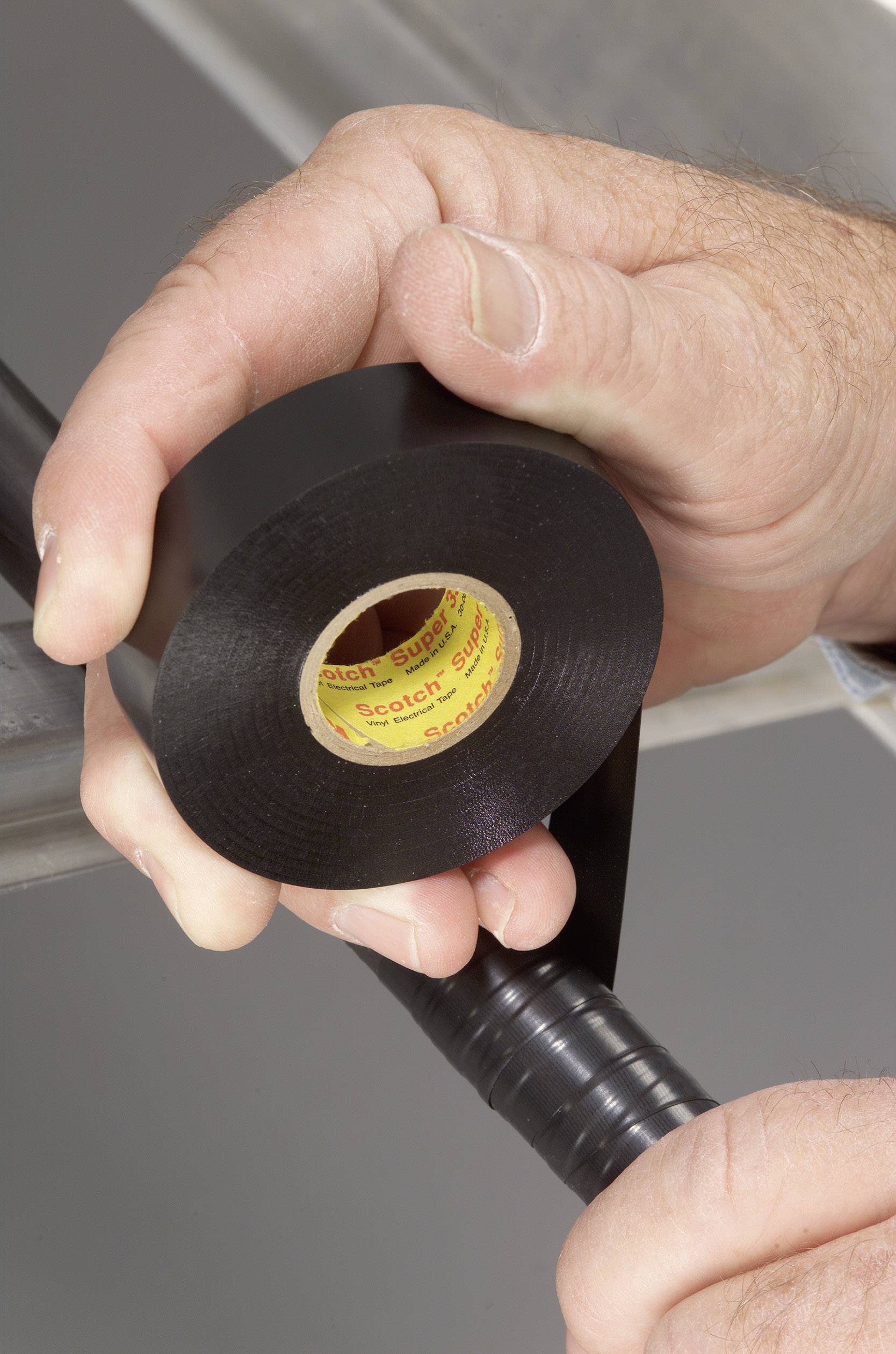 Två händer lindrar svart isoleringsband runt en kabel.