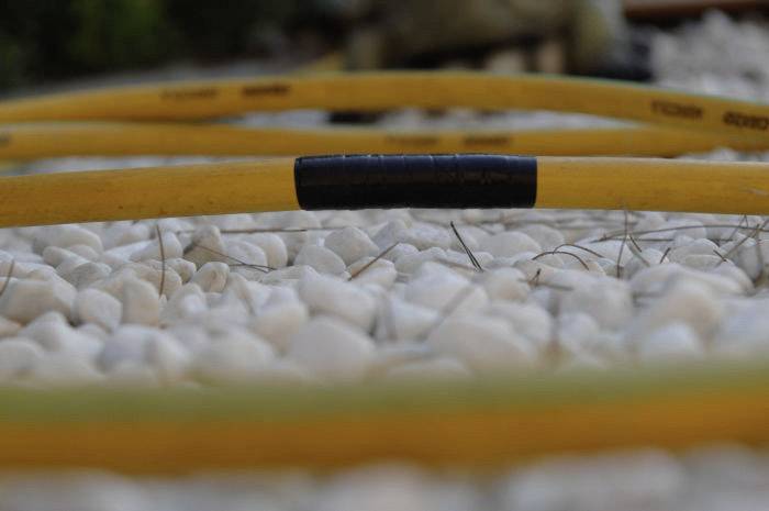 En gul trädgårdsslang ligger på vita kieselstenar. Slangen har ett svart avsnitt. Bakgrunden är lätt oskarp.