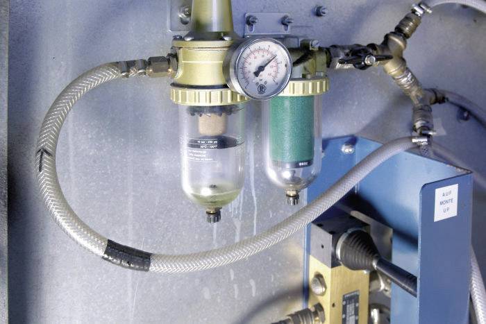 En tryckluftsregulator med manometer och två filter i en teknisk miljö. Kablar och slangar är anslutna.