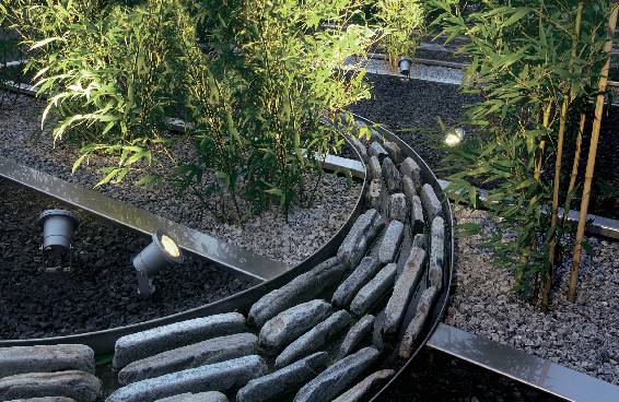 Zen-trädgård med böjd stenmur, bambuplanter och belysning som skapar en lugnande, meditativ atmosfär.